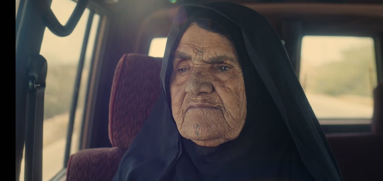 An old woman in a black chador sits in the back of a car