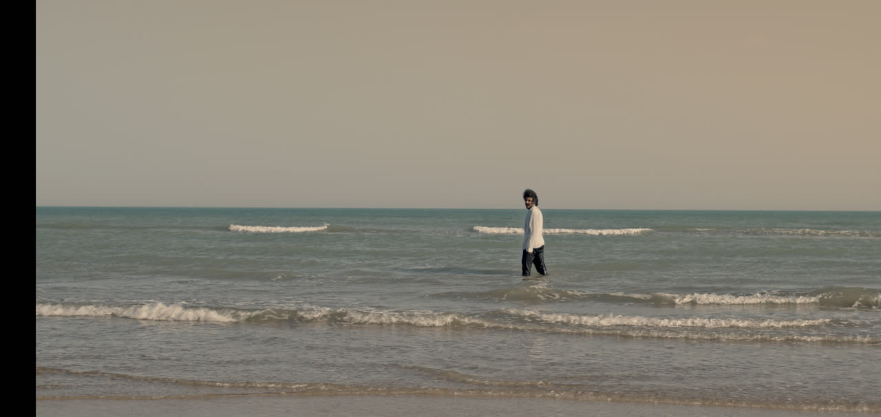 A lone figure stands far out in shallow sea water