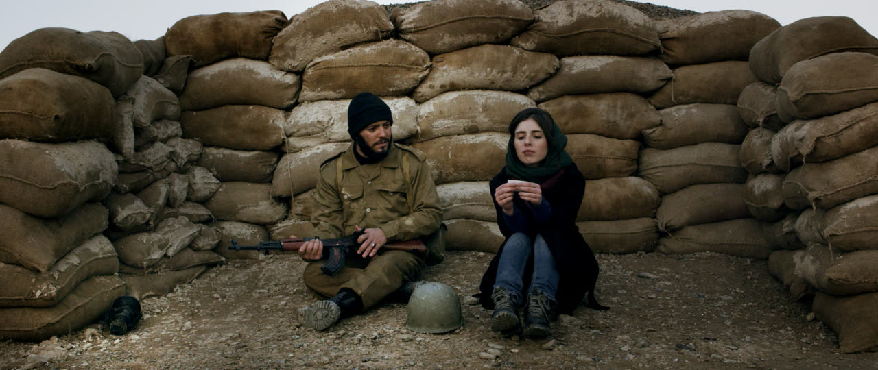 A soldier and a woman sit against a wall of sandbags