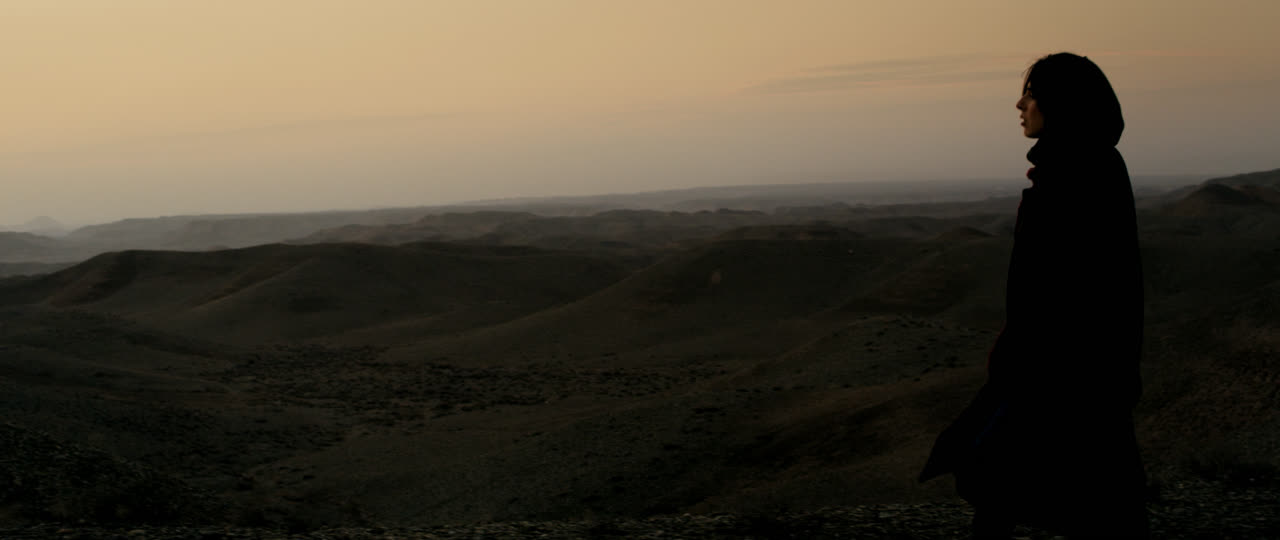A woman in silhouette against a hazy sky over the hills
