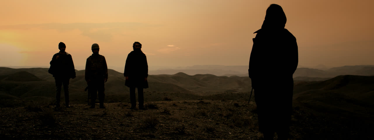 Three soldiers and a woman in silhouette against an orange sunset