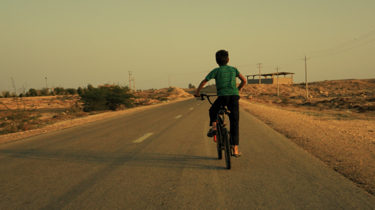 A boy cycles down an empty desert road