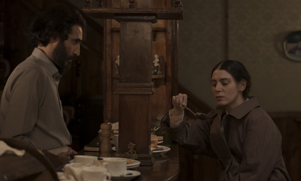 A man stands over a woman eating breakfast at a café table