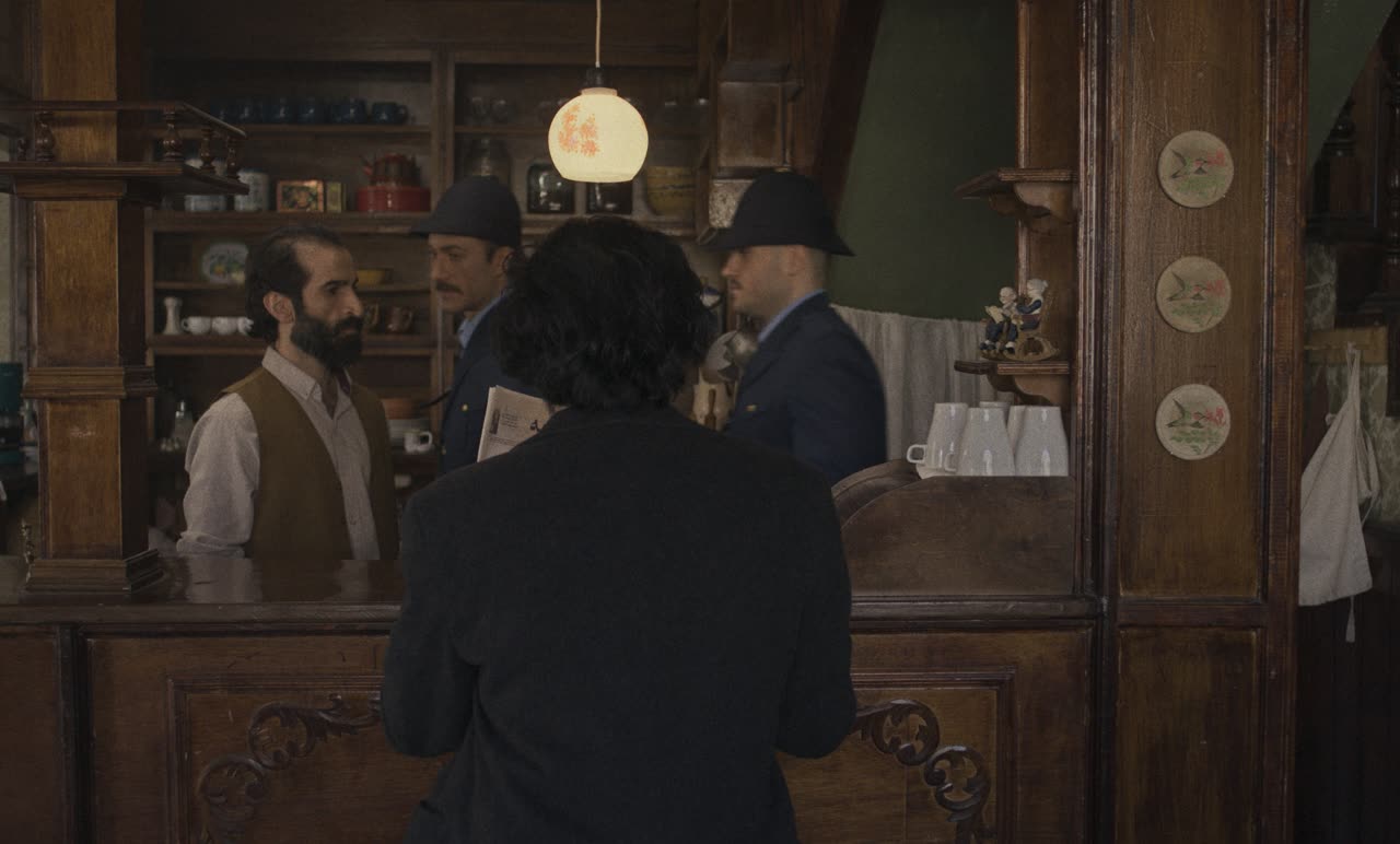 Men in hats talk across the counter of an old café