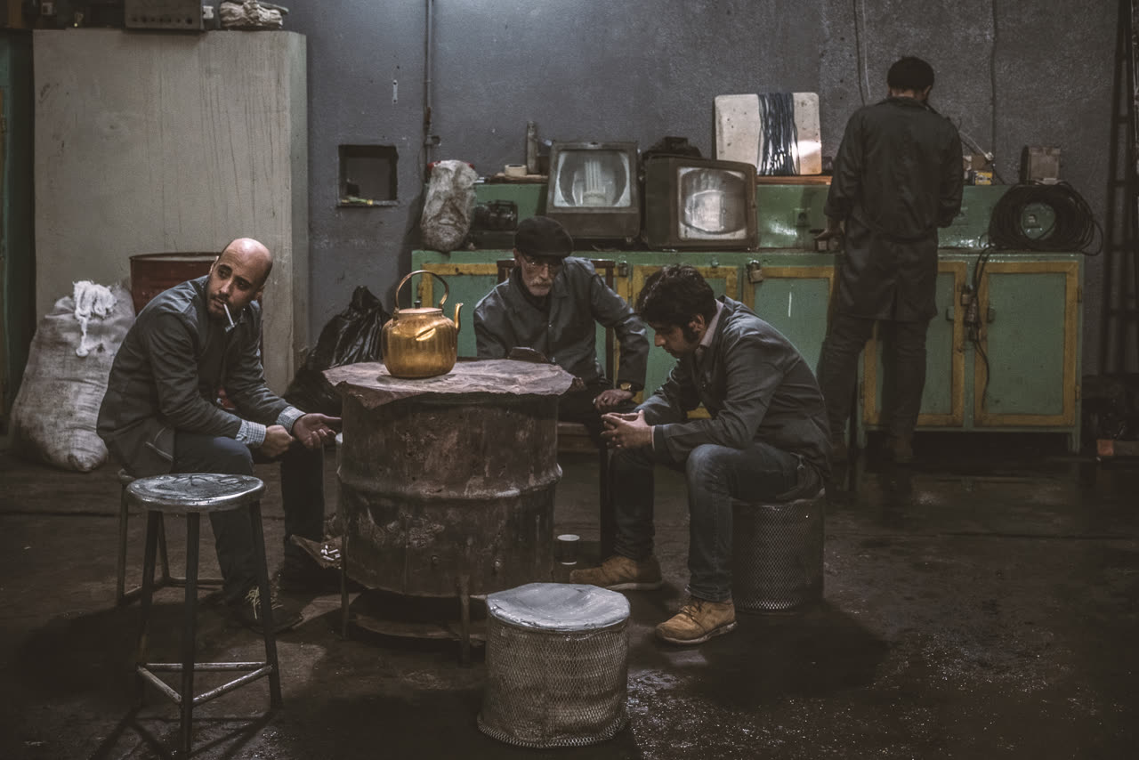 Workers sit around a stove and a teapot inside a factory
