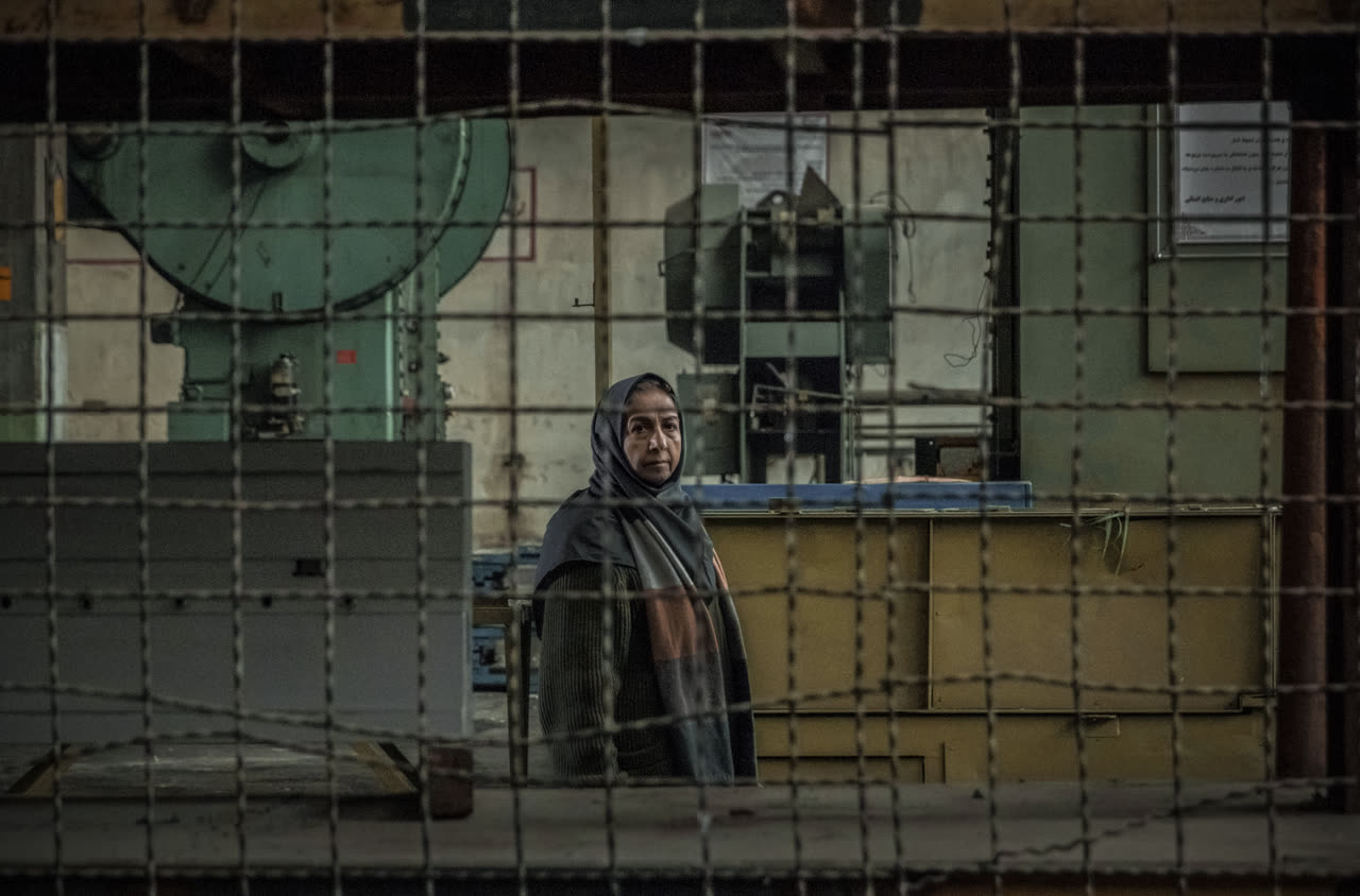 A woman stands behind a wire grid in front of factory machines