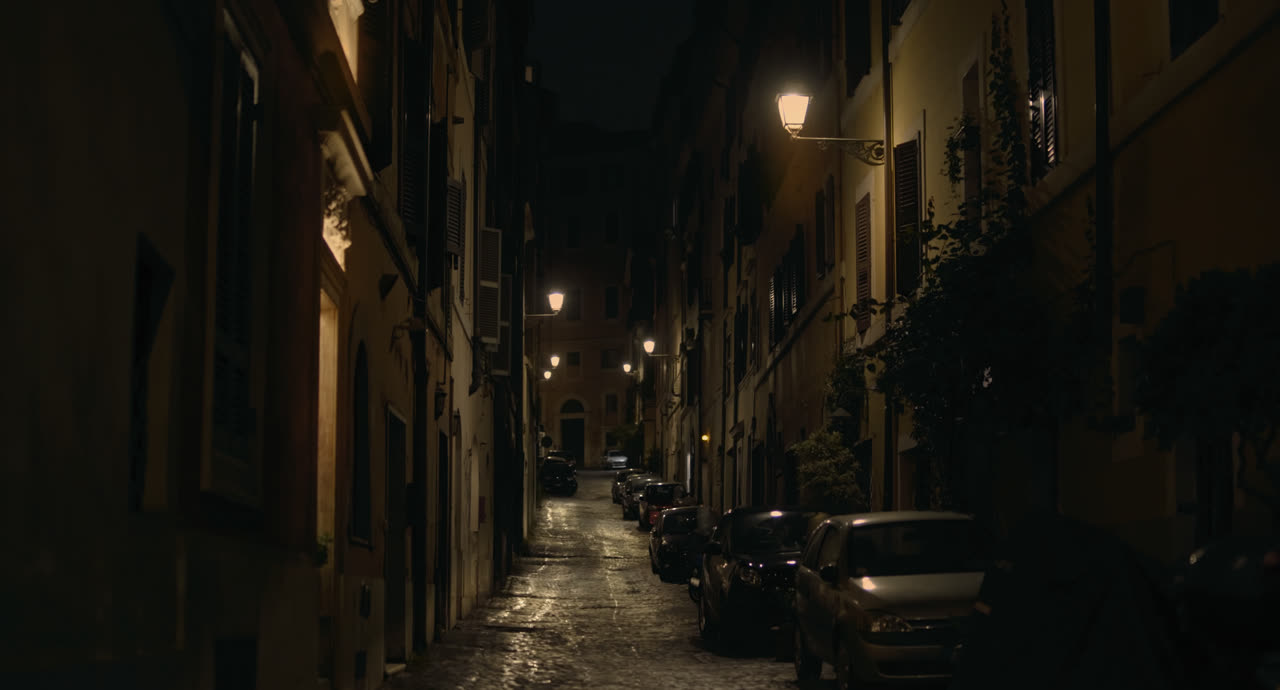A narrow Roman street at night, lit by street lamps