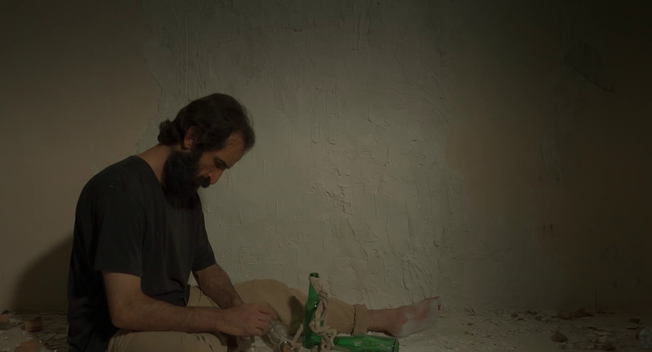 A bearded man sits on a bare floor