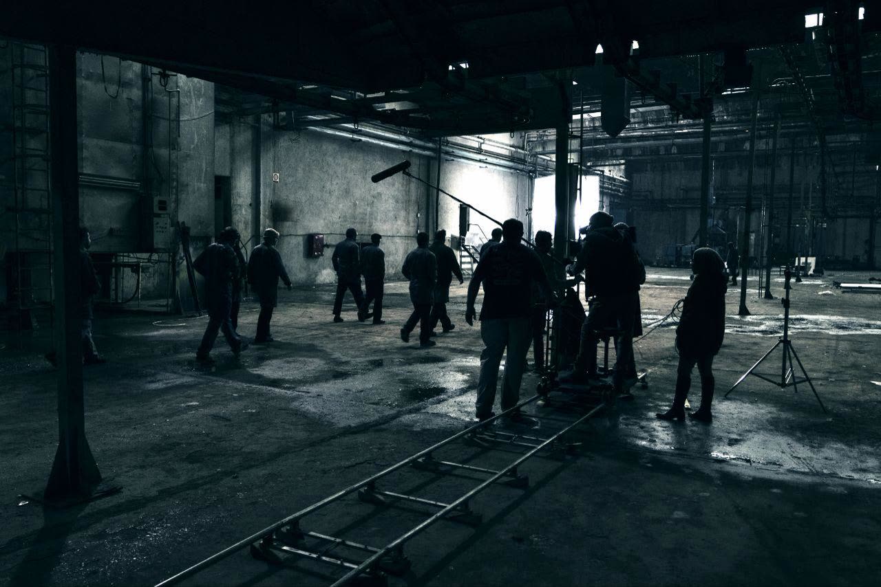 A film crew and camera dolly track on set inside a vast abandoned factory
